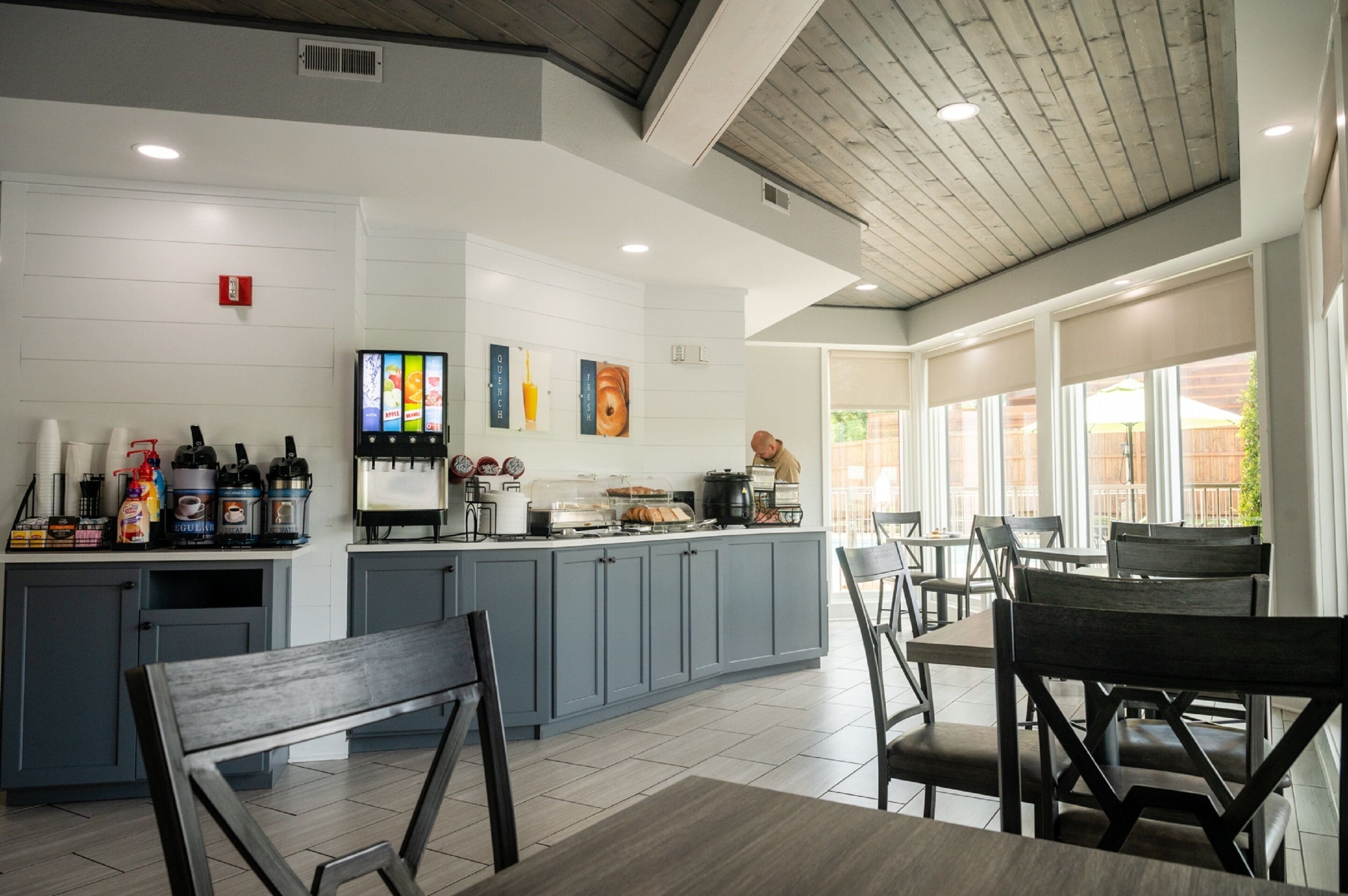 A modern kitchen with grey cabinets, a central island with a coffee machine, and a seating area with wooden chairs and tables.