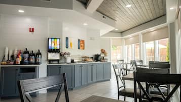 A modern kitchen with grey cabinets, a central island with a coffee machine, and a seating area with wooden chairs and tables.
