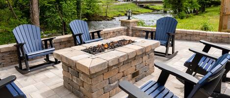 An outdoor patio with Adirondack chairs, a stone fire pit, and a view of a river and bridge.