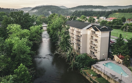 A multi-story hotel with balconies overlooking a river, surrounded by lush greenery and hills.