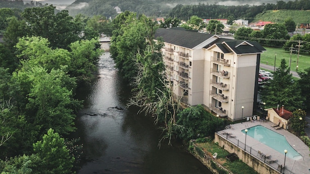 Et hotel med flere etager og balkoner med udsigt over en flod, omgivet af frodig vegetation og bakker.