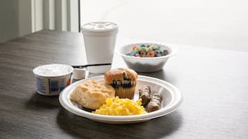A breakfast table with a plate of food, a muffin, a bowl of cereal, and a coffee cup.