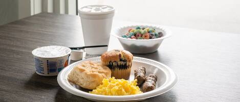 A breakfast table with a plate of food, a muffin, a bowl of cereal, and a coffee cup.