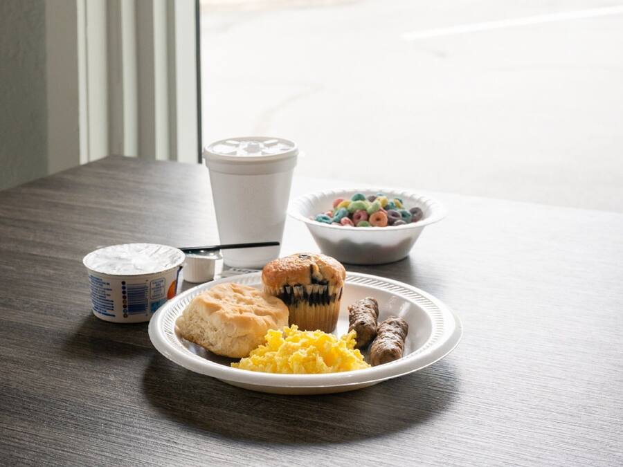 A breakfast table with a plate of food, a muffin, a bowl of cereal, and a coffee cup.