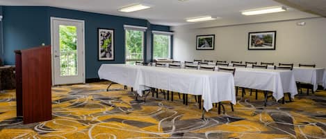 A conference room with a long table, chairs, a podium, and framed pictures on the walls.