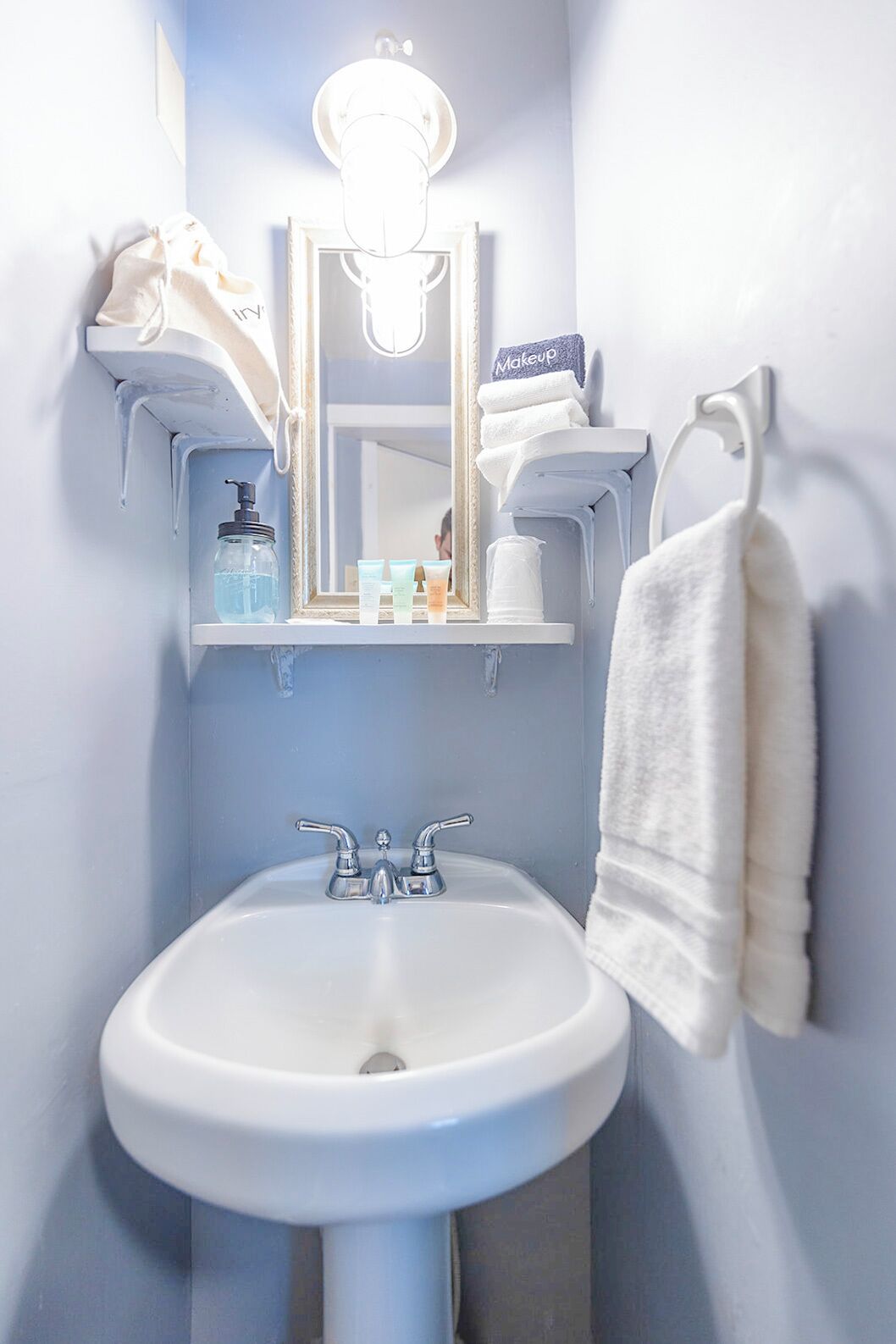 A bathroom with a white sink, a mirror, a towel rack, and a shelf with toiletries.