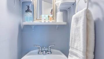 A bathroom with a white sink, a mirror, a towel rack, and a shelf with toiletries.