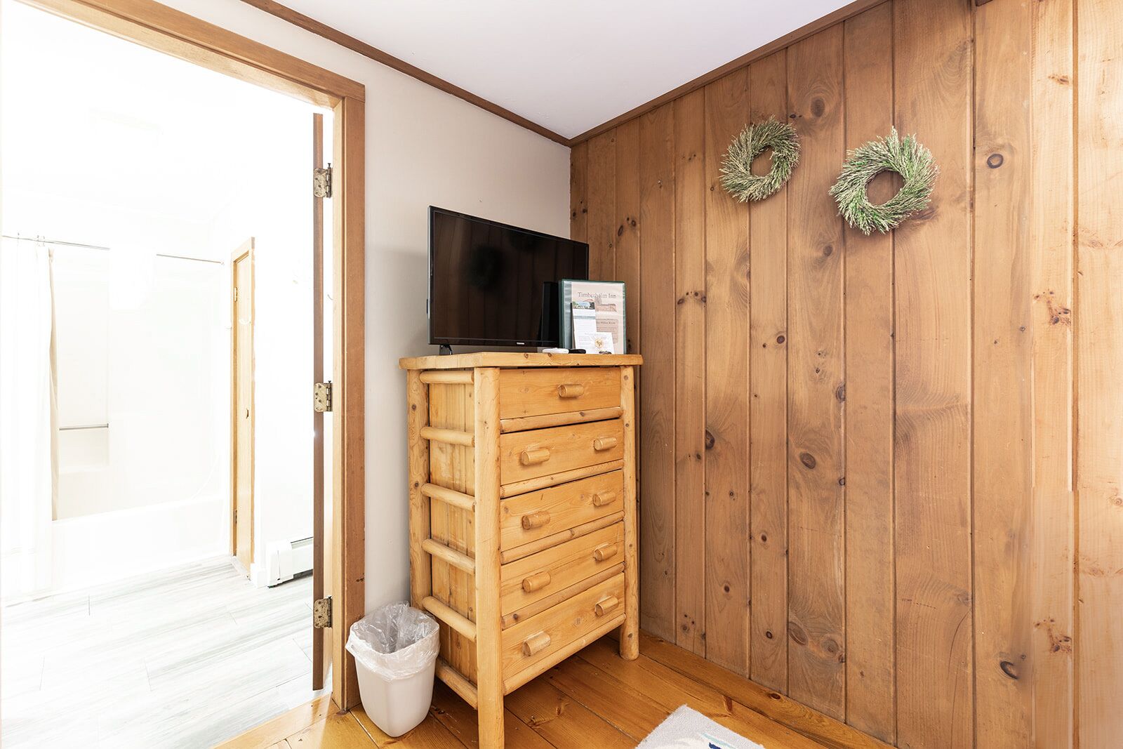 A wooden cabinet with drawers, a television on top, a trash bin, and two wreaths on the wall.