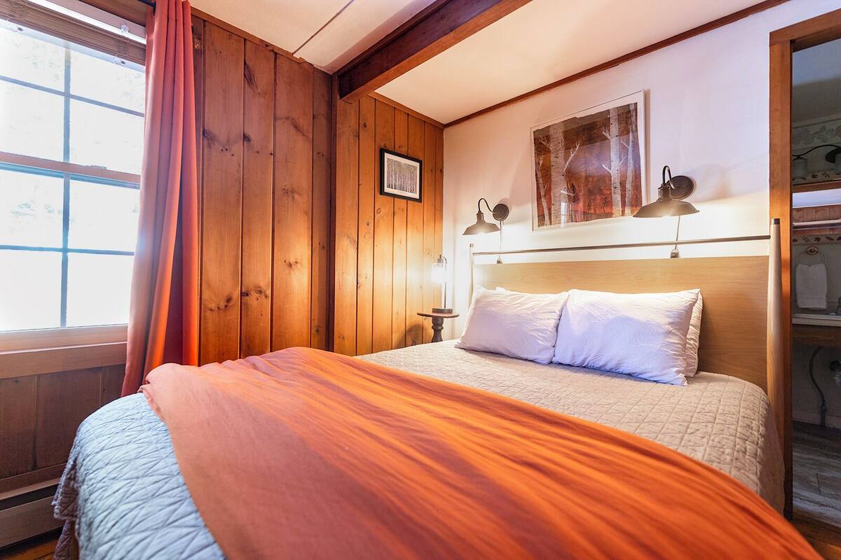 A wooden-paneled room with a bed, a framed picture on the wall, and a window with curtains.