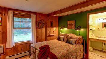 A cozy bedroom with a wooden floor, a large bed with a floral bedspread, a green accent wall, and a window with curtains.