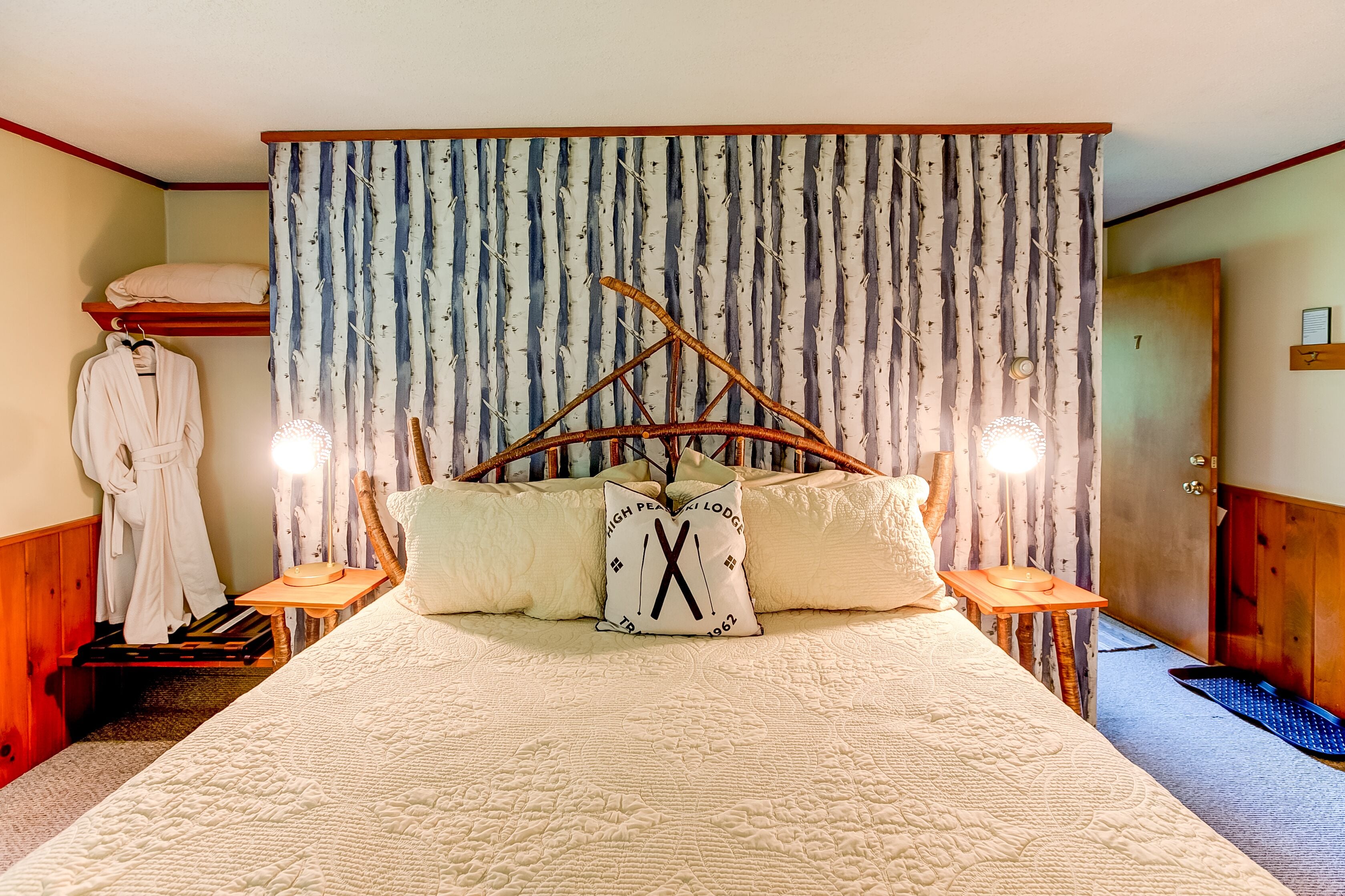 A bedroom with a bed, a wooden headboard, a nightstand, a robe, and a door.