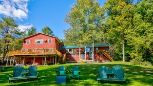 A red cabin with a porch and multiple windows, surrounded by green chairs and a grassy lawn. - Timberholm Inn (Stowe)
