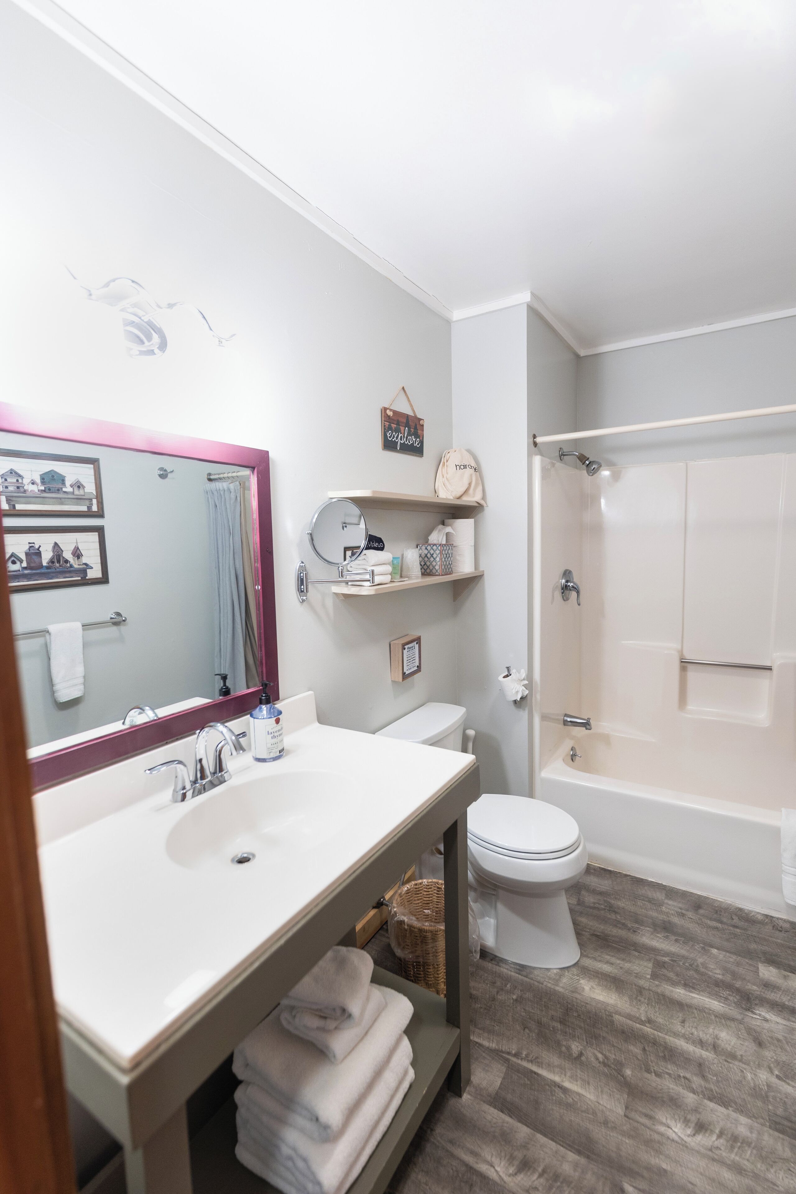 Ein Badezimmer mit weißem Waschbecken, Spiegel und Toilette, einem Duschbereich sowie Holzboden.