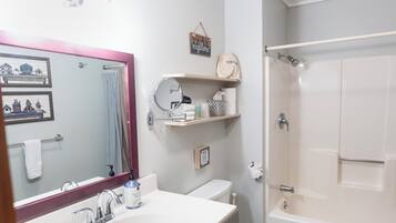 Ein Badezimmer mit weißem Waschbecken, Spiegel und Toilette, einem Duschbereich sowie Holzboden.