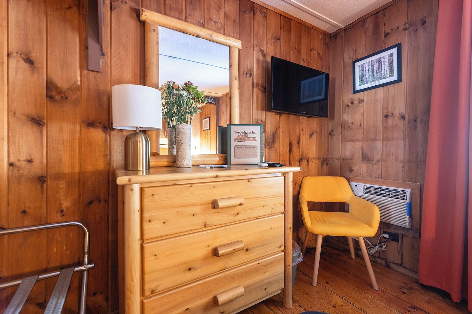 Una habitación de madera con un aparador, una silla, un televisor y un cuadro en la pared.
