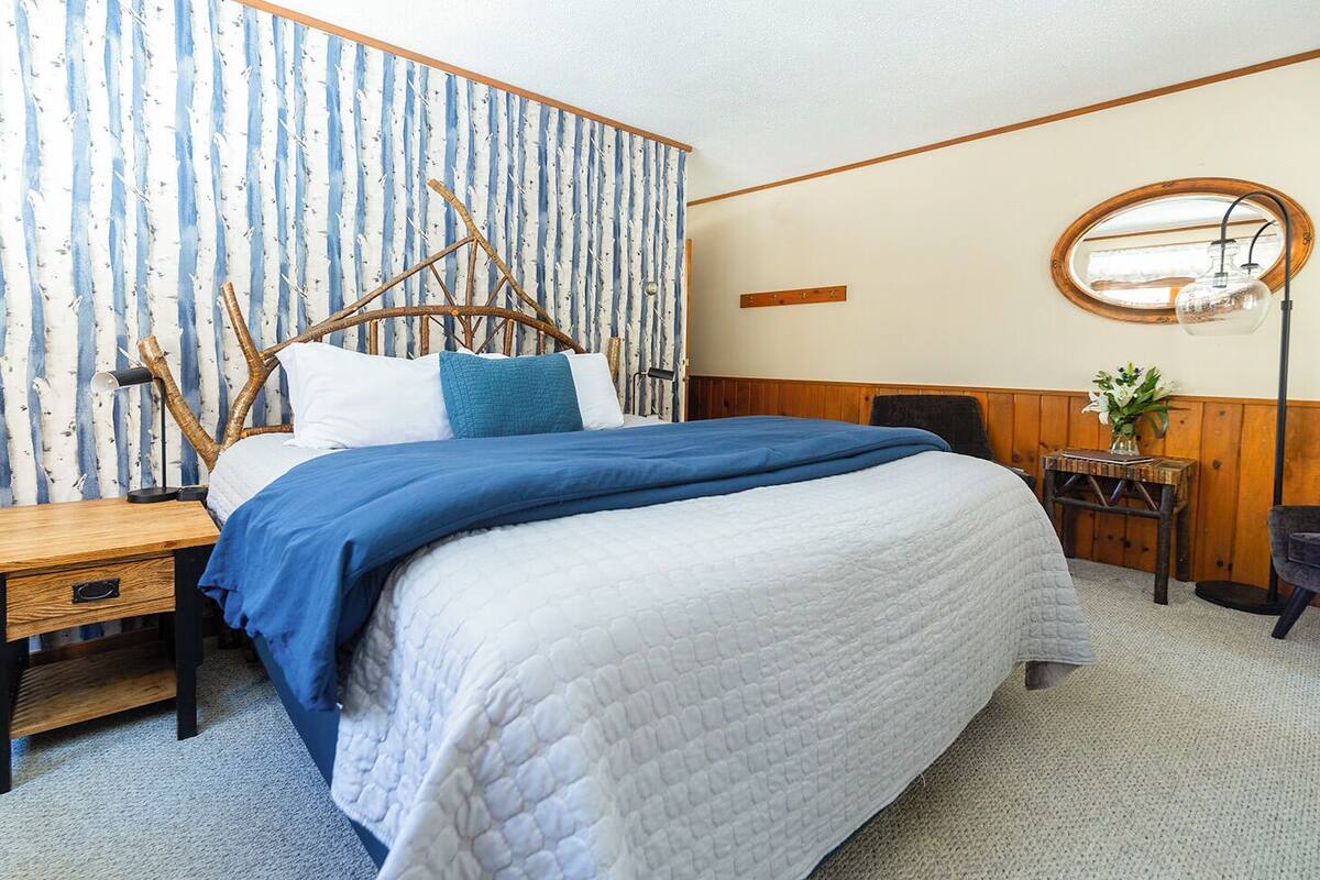 A bedroom with a bed, a nightstand, a mirror, and a small table with a vase of flowers.
