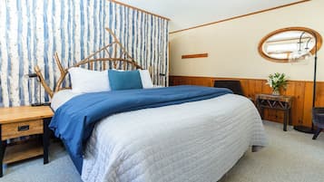 Un dormitorio con una cama, una mesita de noche, un espejo y una pequeña mesa con un florero.