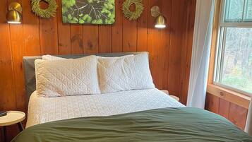 A wooden-paneled bedroom with a bed, two wall-mounted lamps, and two wreaths on the wall.
