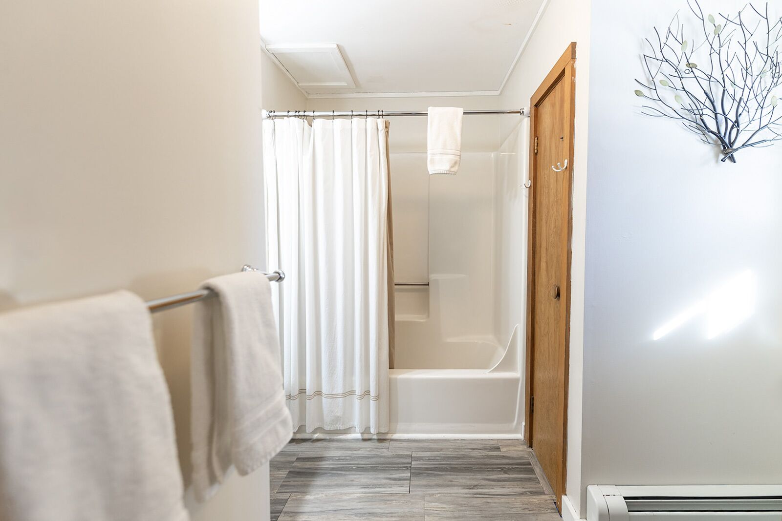 A narrow hallway with a shower area, a wooden door, and a wall-mounted light fixture.