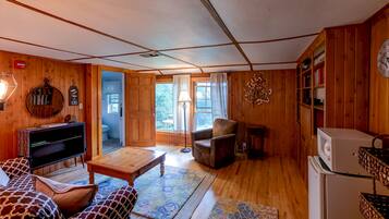 A cozy wooden interior with a sofa, a television, a wooden table, and a refrigerator.