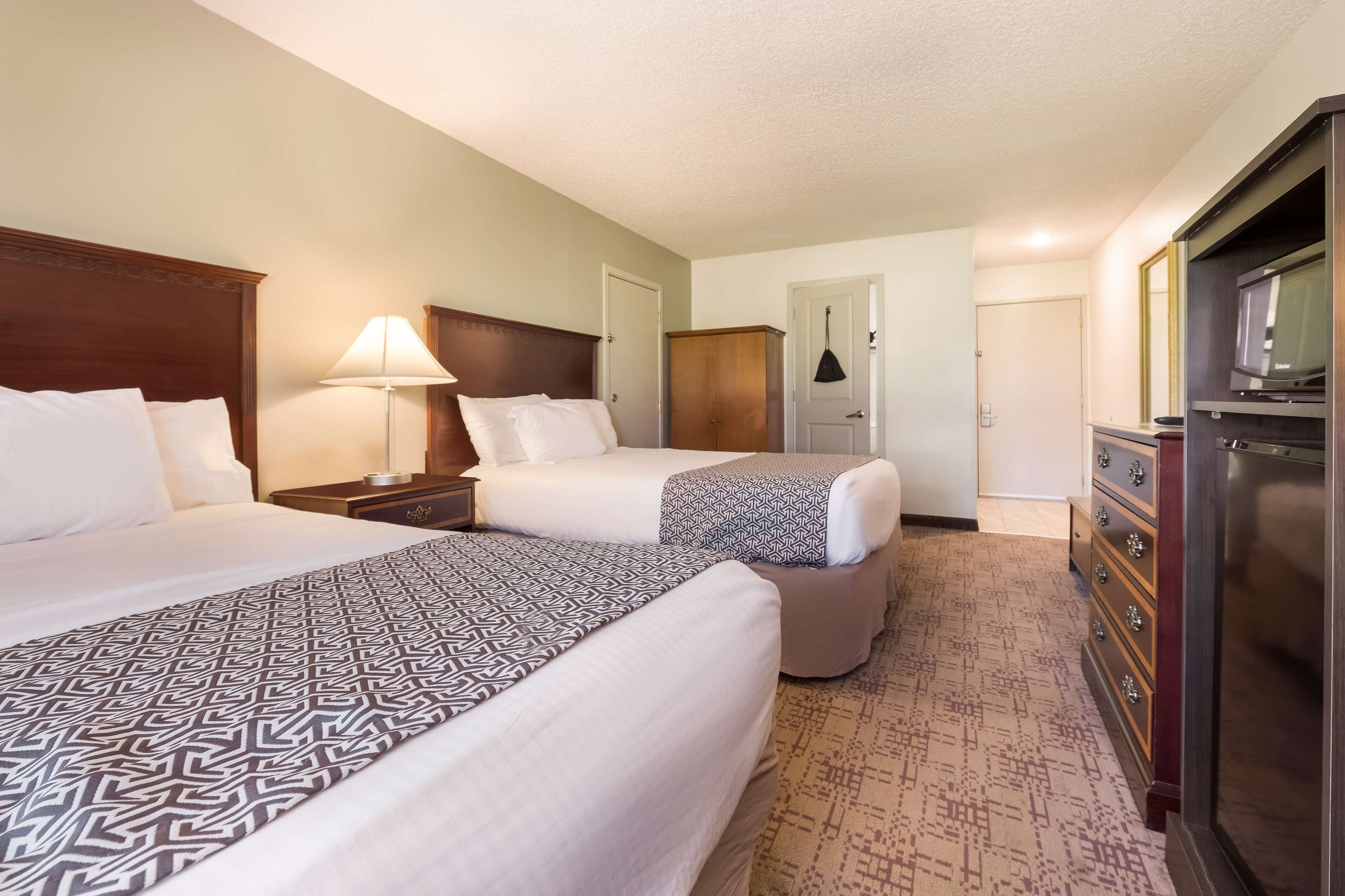 A hotel room with two beds, a dresser, a television, and a lamp.