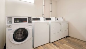 A laundry area with a front-loading washing machine, a dryer, and two stacked dryers. - SureStay Hotel by Best Western Thomson (Thomson)