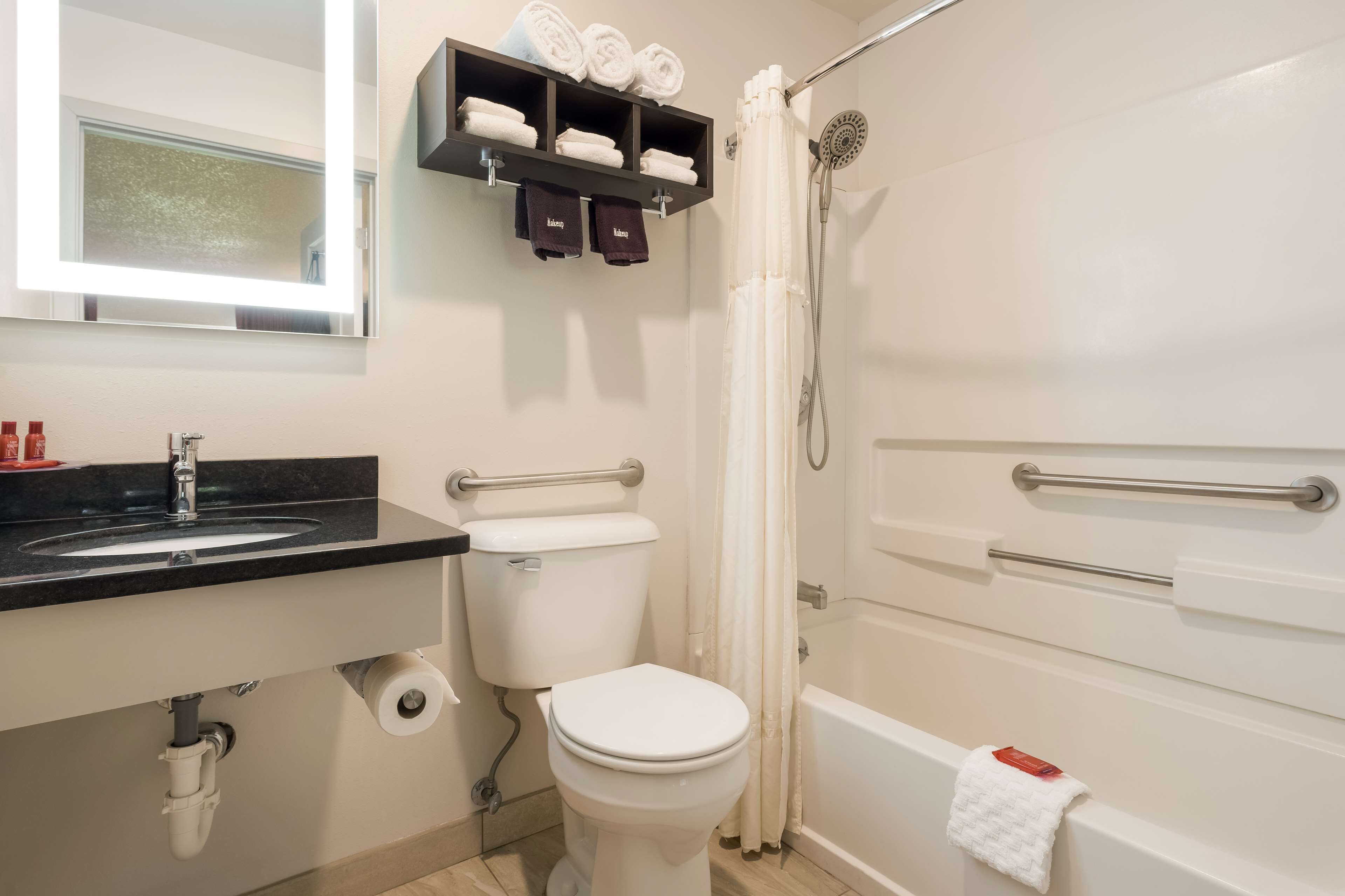 A bathroom with a sink, toilet, and bathtub. There are towels and toiletries on the shelf.