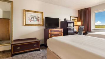 Habitación de hotel con cama, televisor, escritorio con lámpara y ventana con vista al exterior.