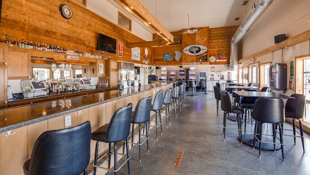 A bar area with a long counter, bar stools, and a variety of liquor bottles. - SureStay Hotel by Best Western Thomson (Thomson)
