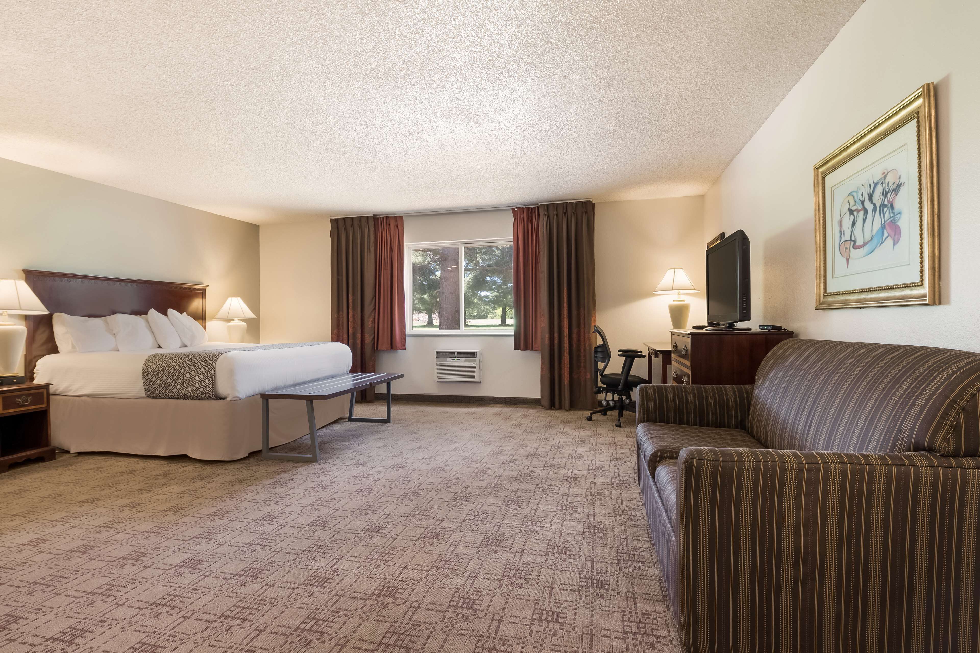 A hotel room with a bed, a sofa, a desk, and a window with curtains.