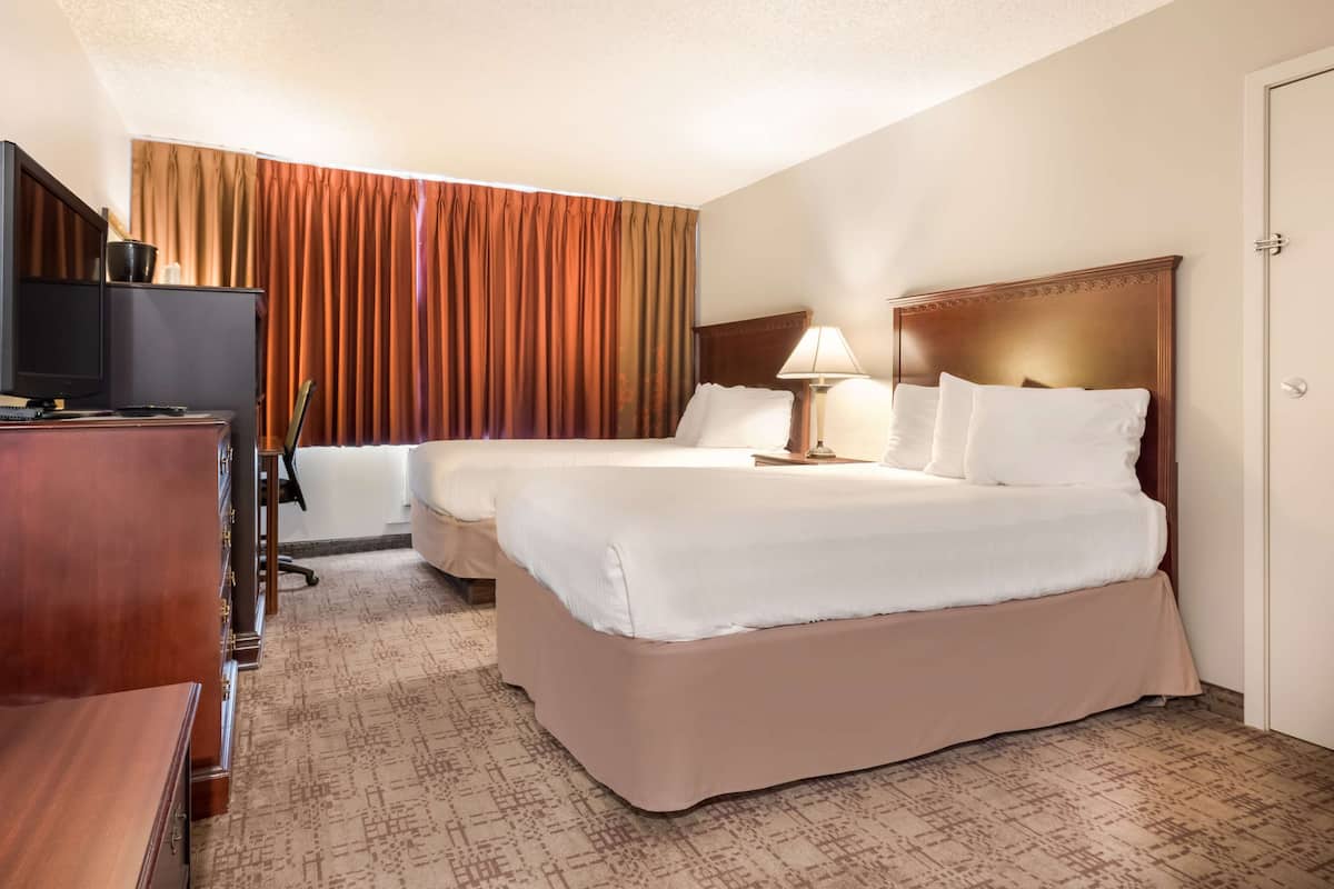 A hotel room with two beds, a desk with a television, and a window with curtains.