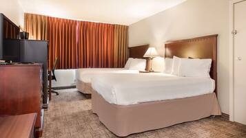 A hotel room with two beds, a desk with a television, and a window with curtains.