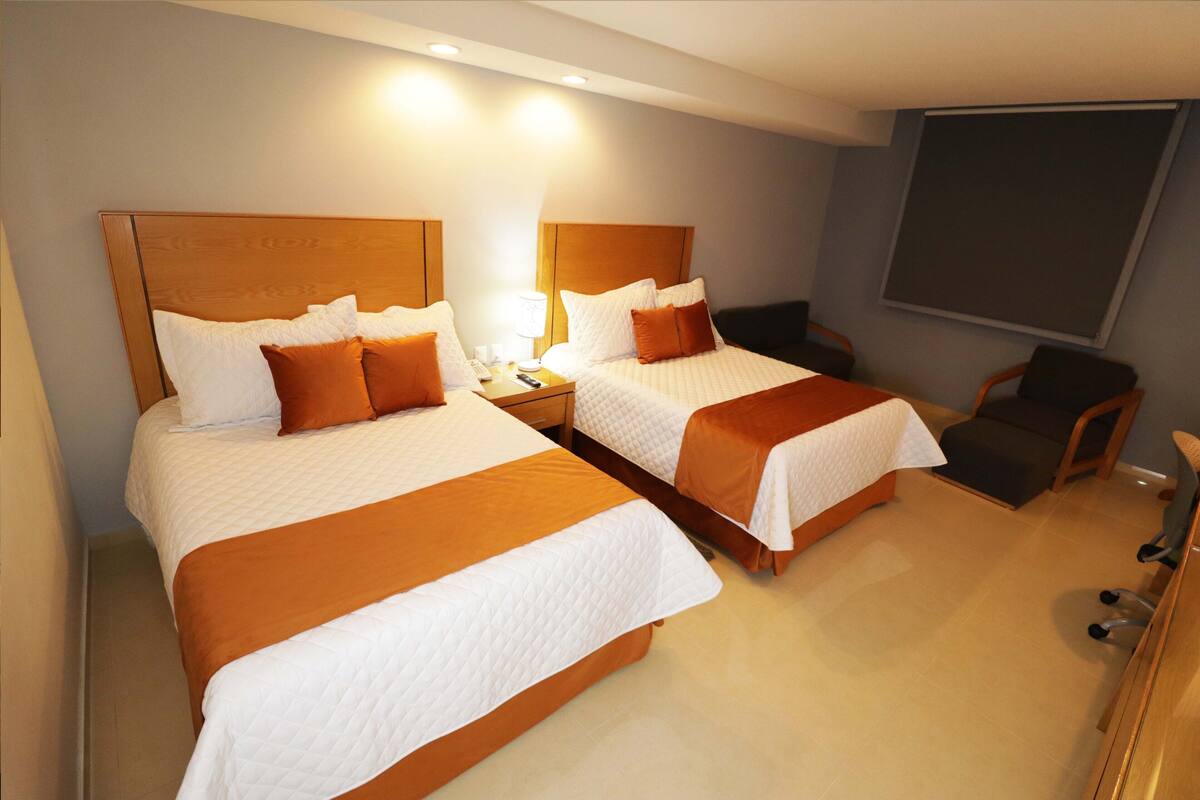Ein Hotelzimmer mit zwei Betten, einem Schreibtisch, einem Stuhl und einem großen Fenster.