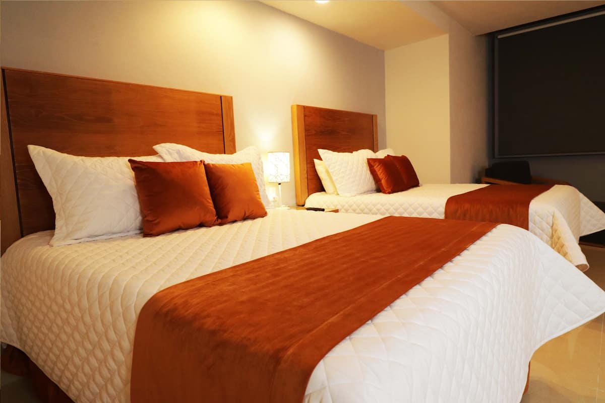 Ein Hotelzimmer mit zwei Betten, jeweils mit einem hölzernen Kopfteil, weißer Bettwäsche und braunen Tagesdecken.