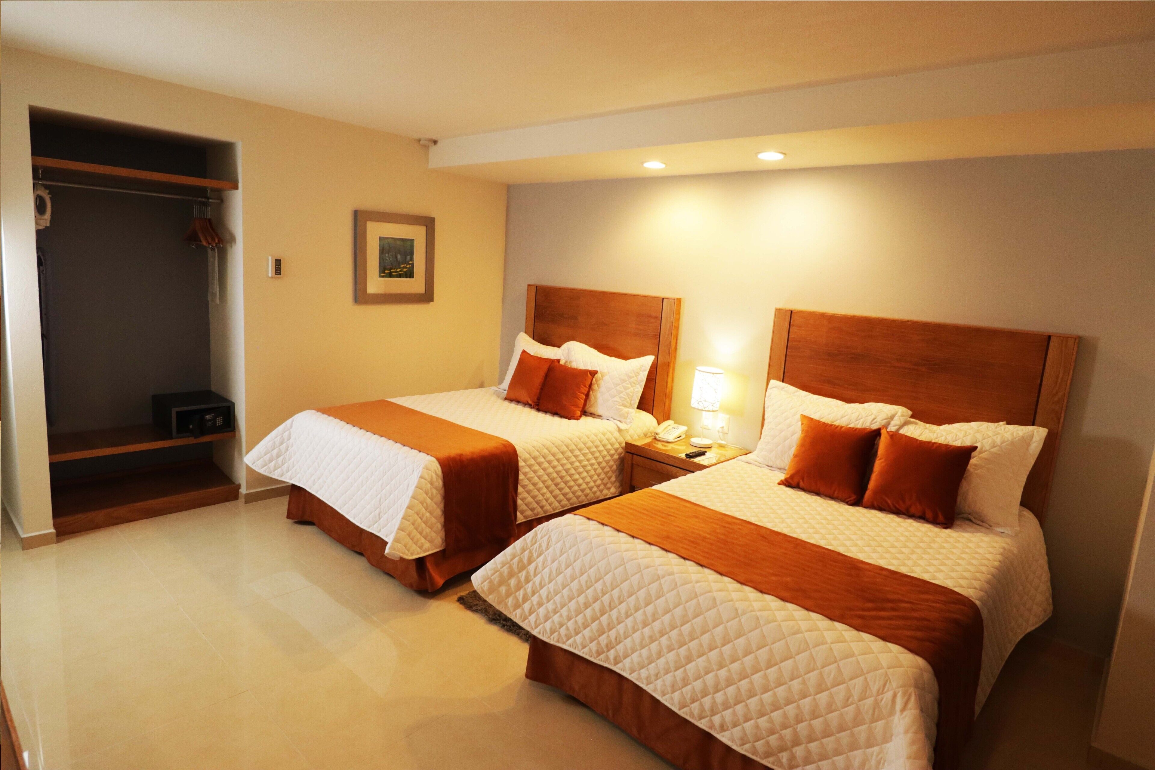 Habitación de hotel con dos camas, un armario, una mesita de noche con lámpara y un cuadro en la pared.