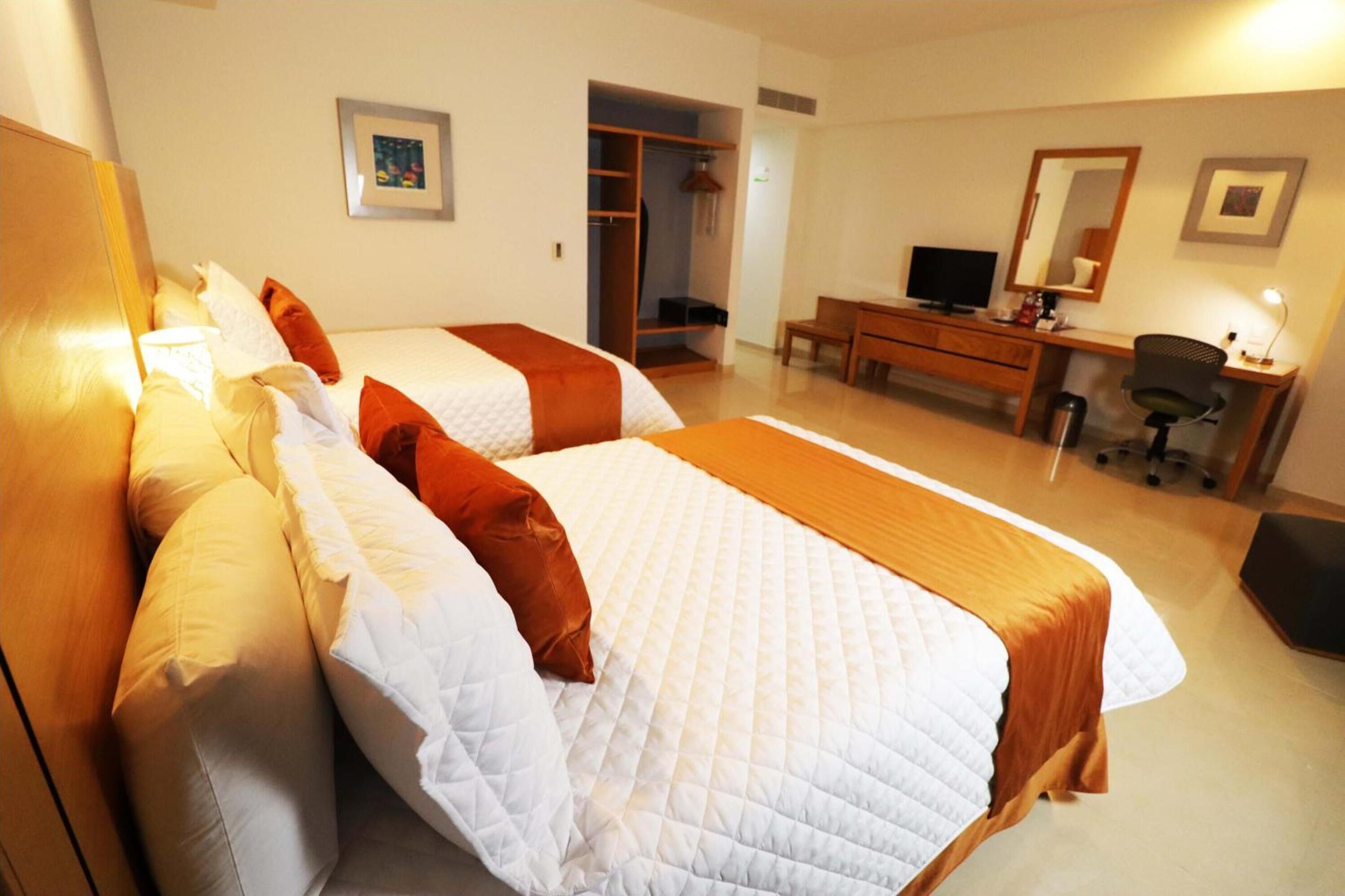 Habitación de hotel con dos camas, un escritorio, una silla, un televisor y un armario.