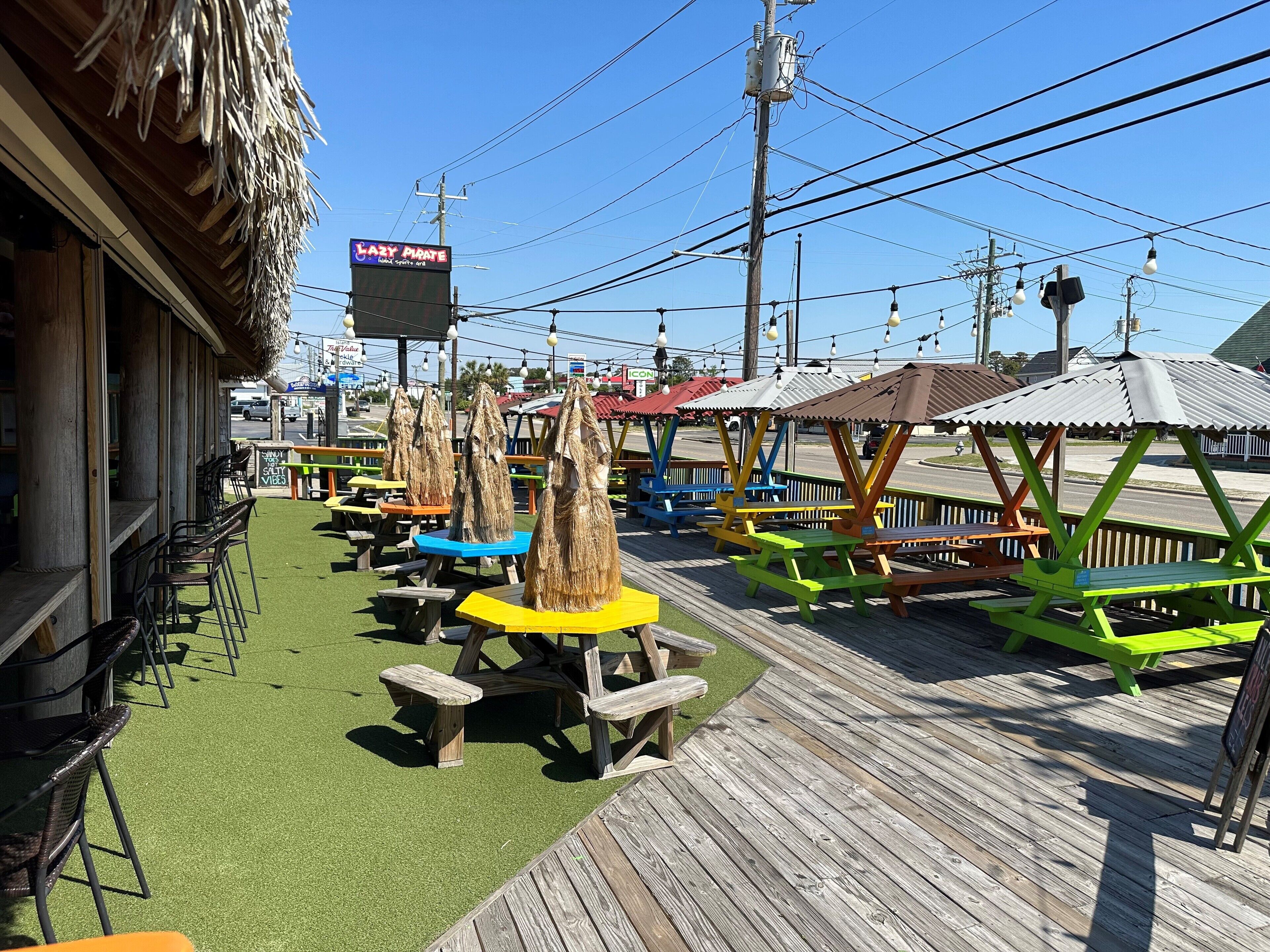 A wooden deck with picnic tables and benches, a thatched-roof building, and a sign for 'Lazy Pirate'.