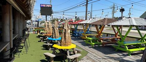 A wooden deck with picnic tables and benches, a thatched-roof building, and a sign for 'Lazy Pirate'.