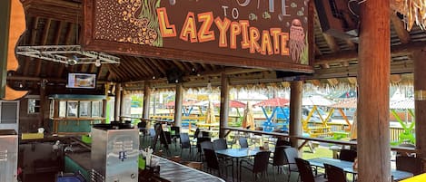 Un restaurant avec une enseigne indiquant « Bienvenue au Lazy Pirate », des tables en plein air et un espace bar.