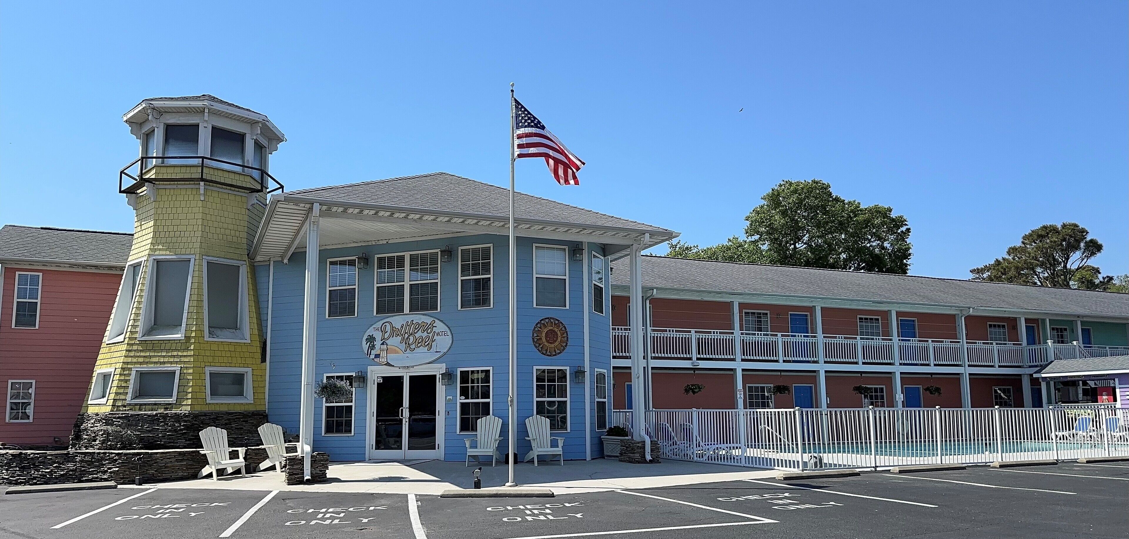A building with a lighthouse tower, a sign reading "The Drifters Reef Motel," and a flagpole with an American flag.