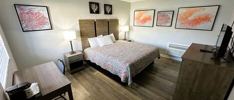 A hotel room with a bed, bedside tables, a desk, and artwork on the walls.