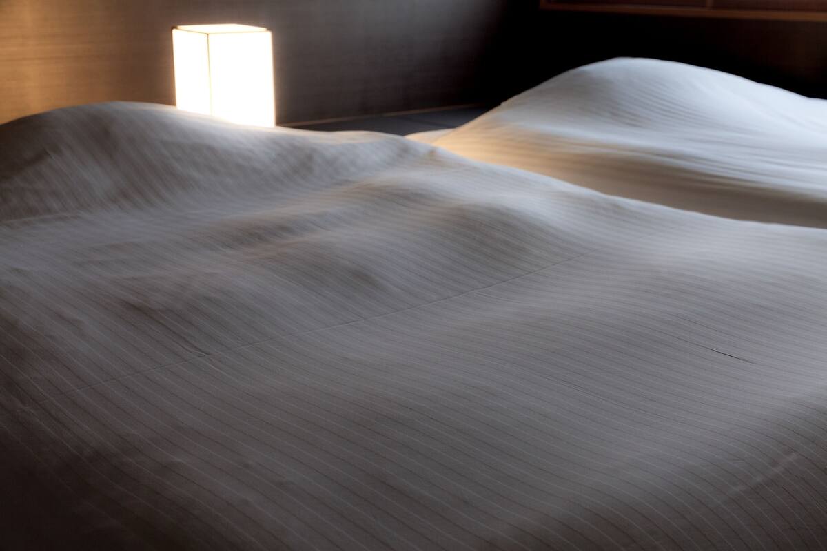 A bed with a textured white cover, a bedside lamp, and a wooden headboard.
