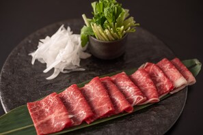 A plate with thinly sliced red meat, shredded white vegetables, and a small bowl of green leafy vegetables.