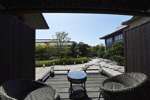 A wooden deck with wicker chairs and a table, overlooking a landscaped garden with a stone path and greenery.
