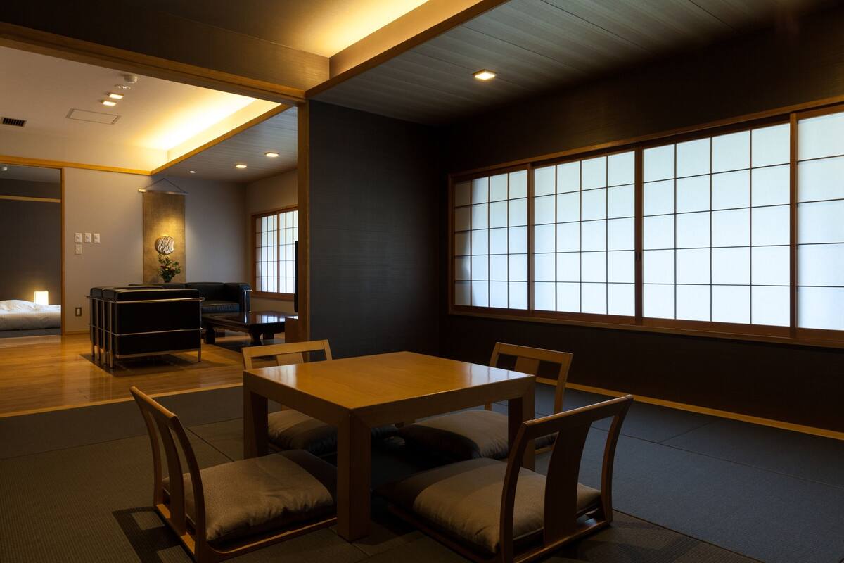 A traditional Japanese-style room with tatami flooring, a low wooden table with cushions, and a sliding shoji screen window.