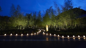 Un chemin bordé de lanternes illuminées menant à un bâtiment, lui-même entouré d’arbres.