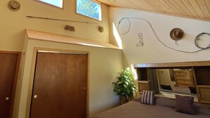 Una habitación con techo de madera, un ventanal grande, una puerta, una planta y una cama con almohadas.