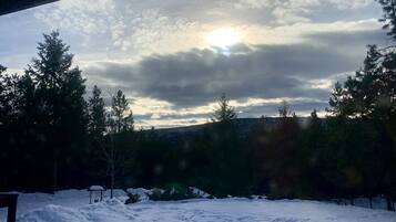 A snowy landscape with a view of the sun peeking through clouds, surrounded by trees.