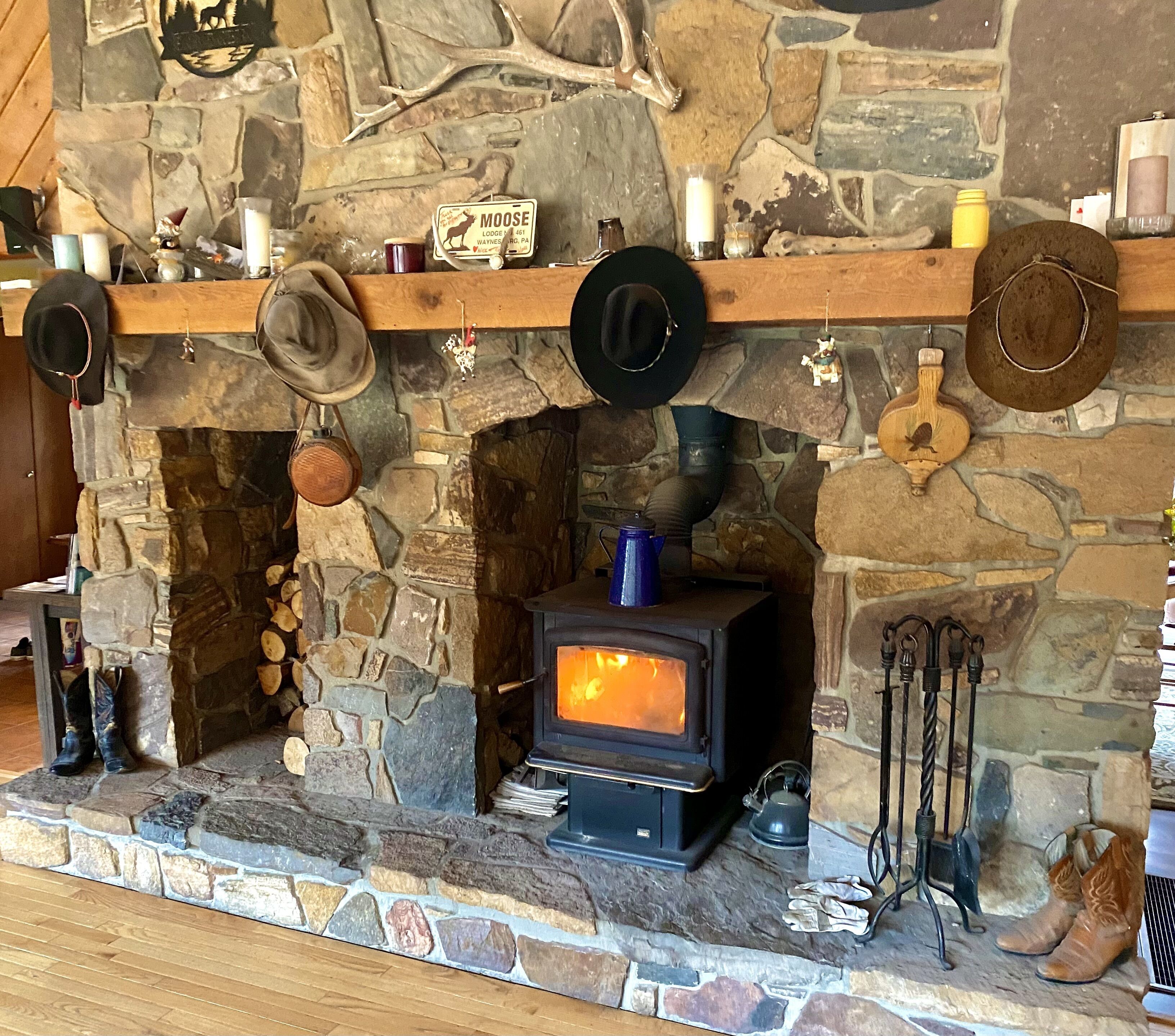 Una chimenea de piedra con estufa de leña, colocada sobre una pared de piedra con diversos objetos decorativos.