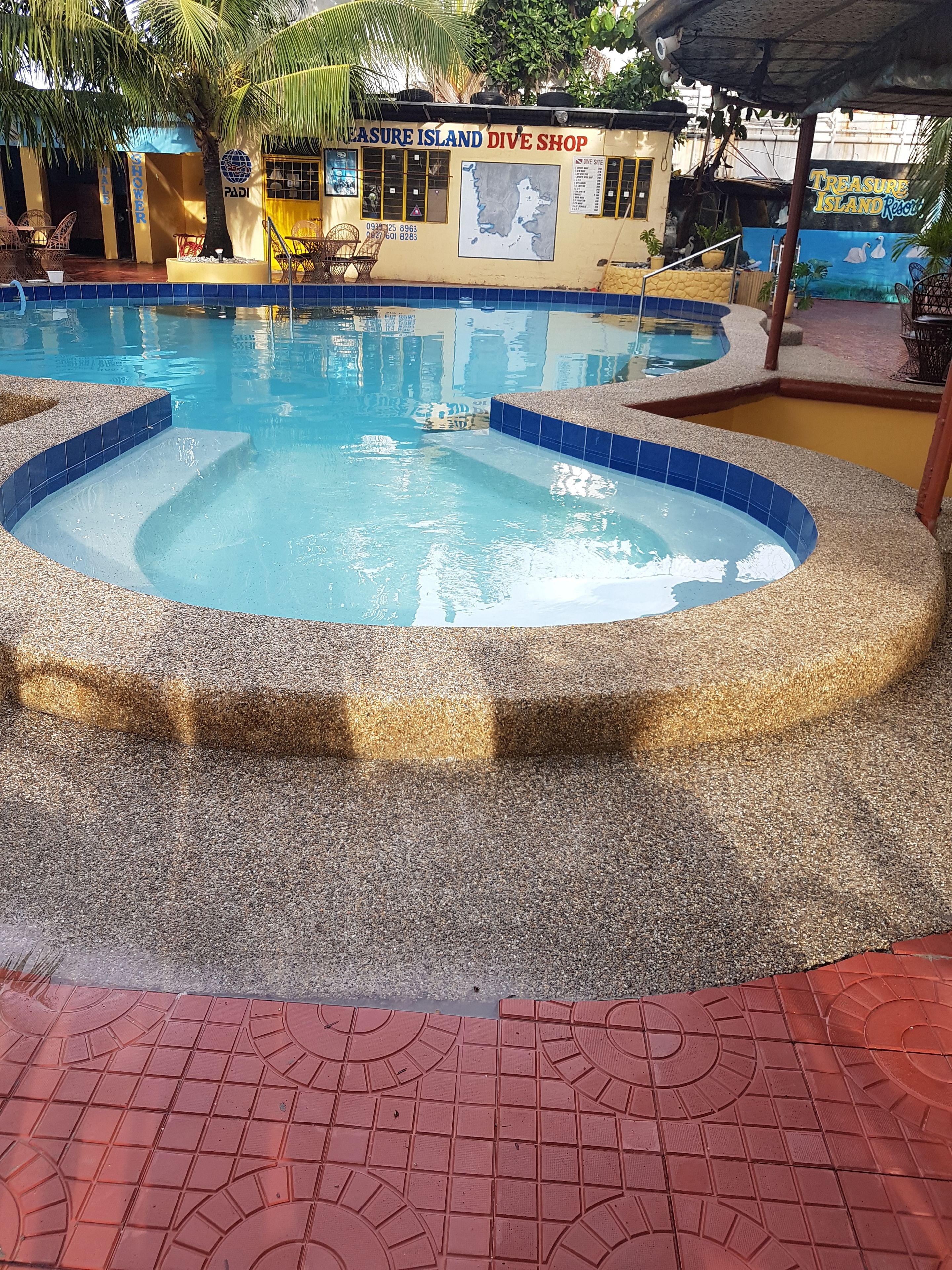 A swimming pool with a blue and beige tiled design, surrounded by a pebble-like texture.